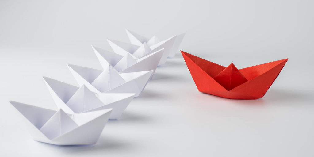 Image of 5 white paper boats and 1 red paper boat