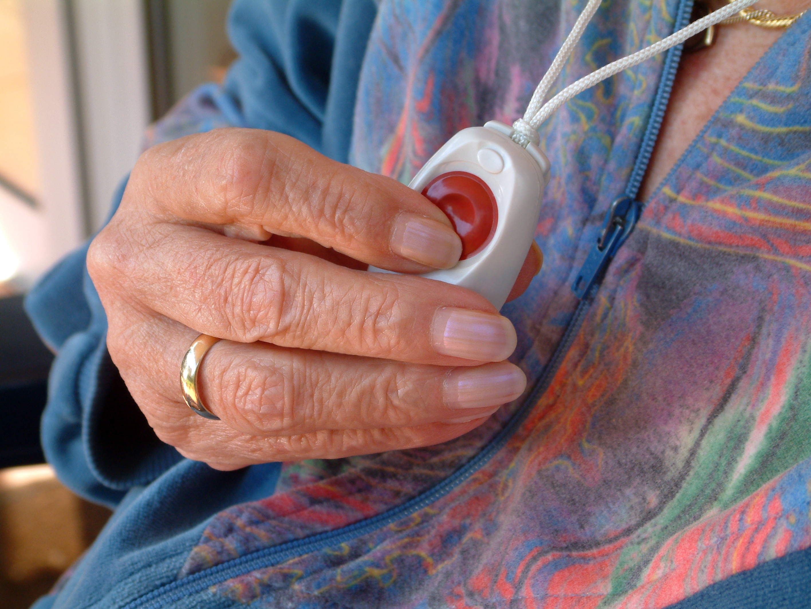 Elderly woman's hand holding a Telecare alarm pendant