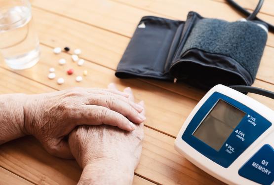 Old lady checking blood pressure, medical tablets on table