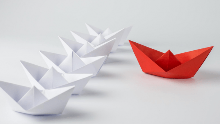 Image of 5 white paper boats and 1 red paper boat