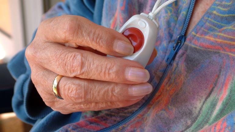 Elderly woman's hand holding a Telecare alarm pendant